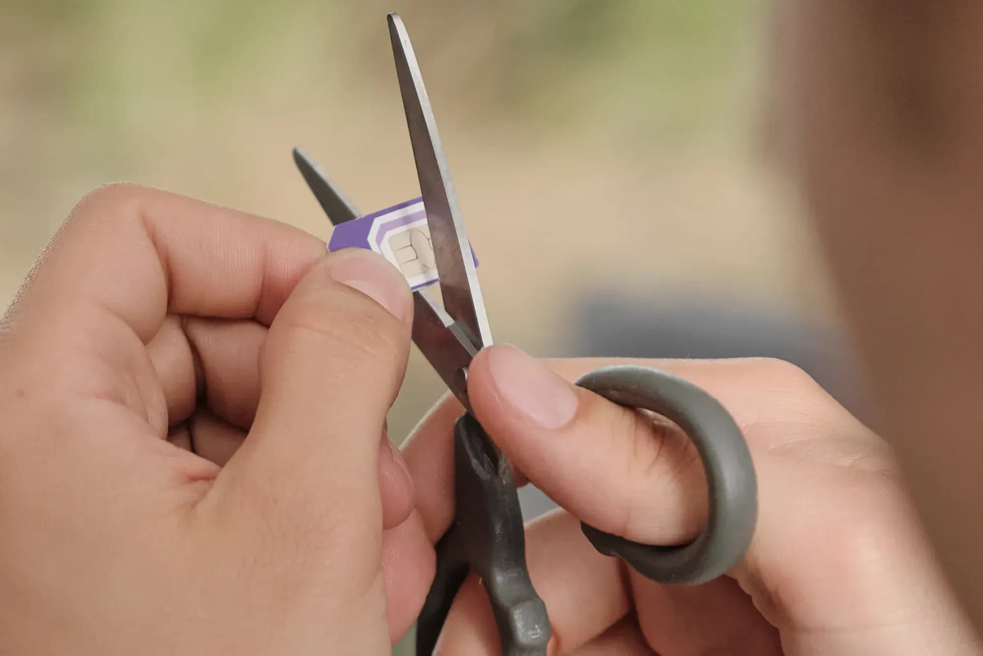 Close-up of hands cutting a SIM card with a pair of scissors.