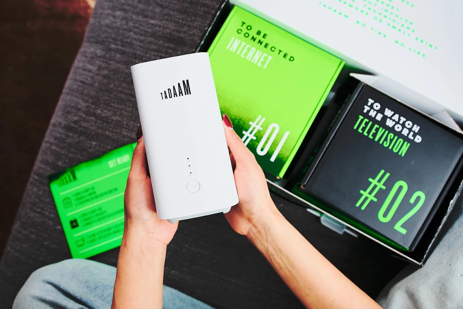 Person holding TADAAM Modem with in the background the TADAAM Box laying open.