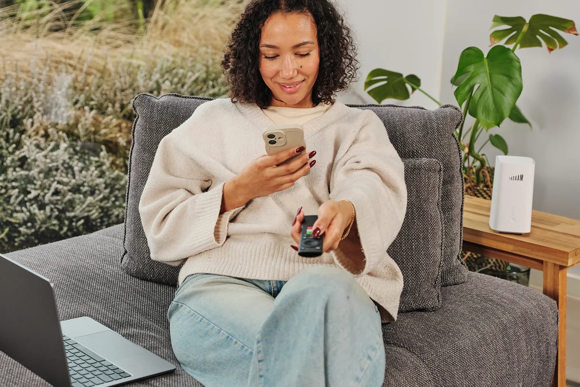 An image of a woman sitting on the couch with a Macbook laptop on her lap and a TADAAM's modem next to her.