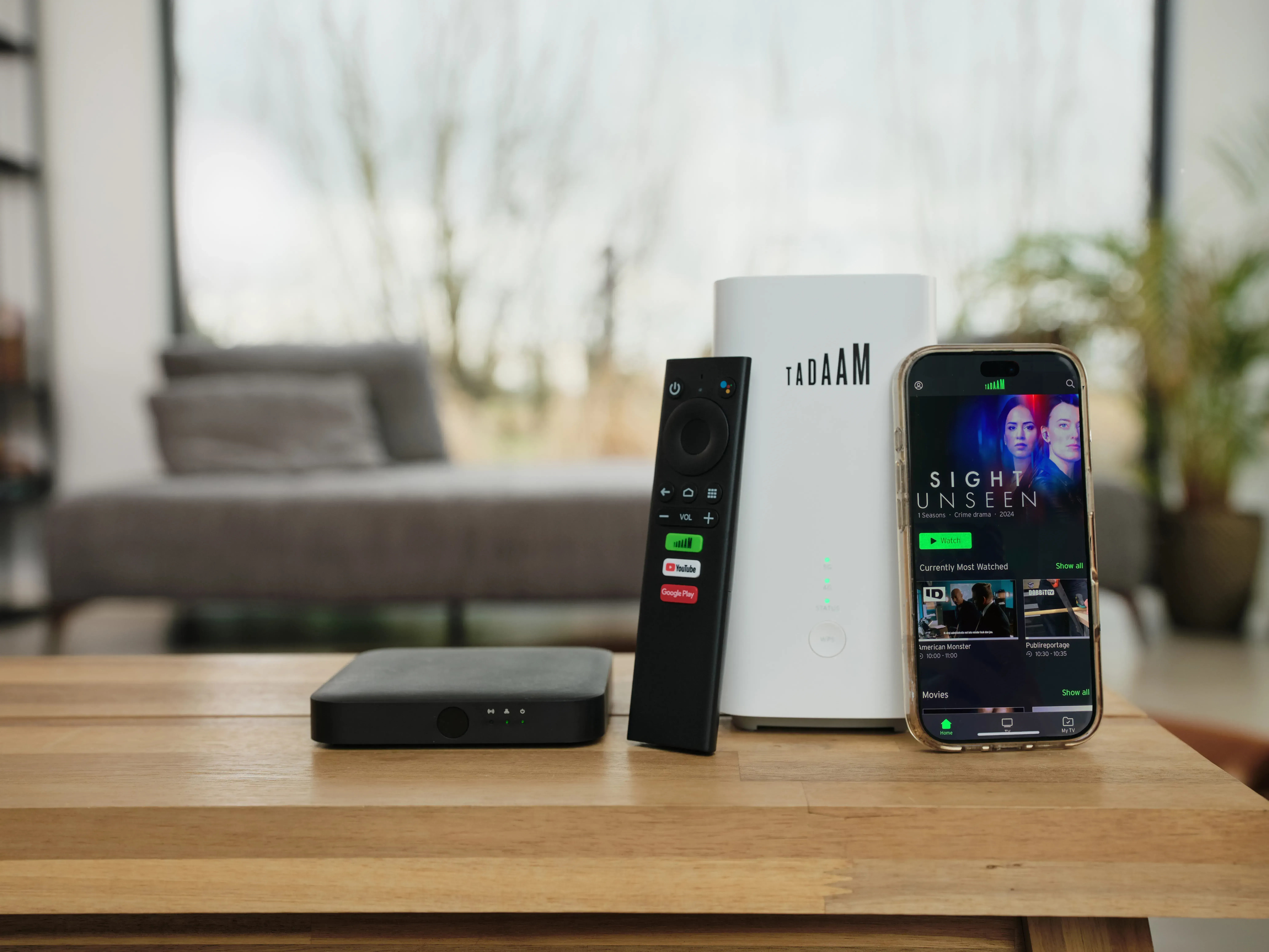 TADAAM modem, TV box, and remote control displayed on a table next to a smartphone showing the TADAAM TV app.